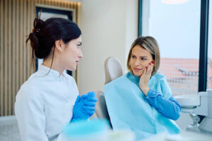 Female patient experiencing a painful toothache, holding her cheek, discussing symptoms with the dentist in a modern dental clinic